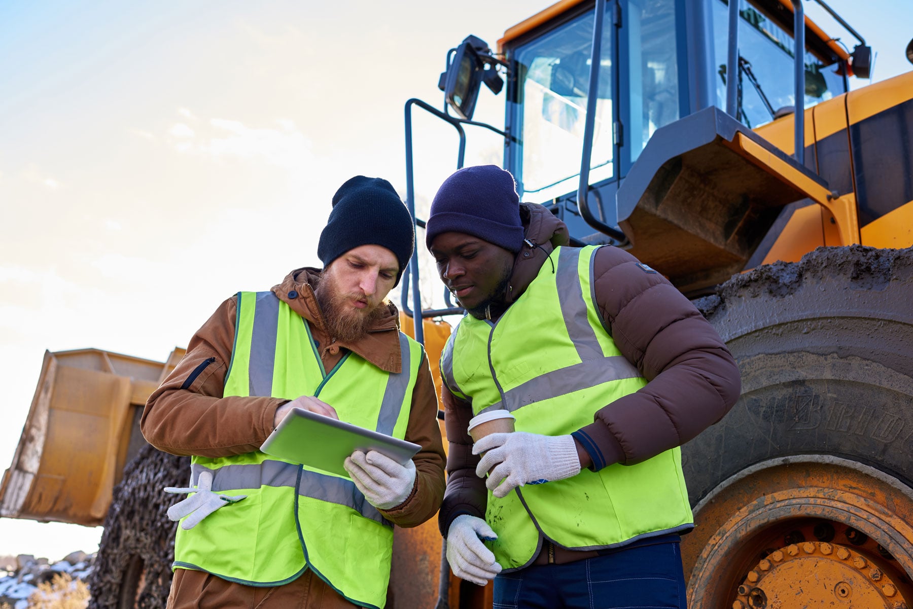 Crew workers looking at tablets, standing next to a heavy machinery